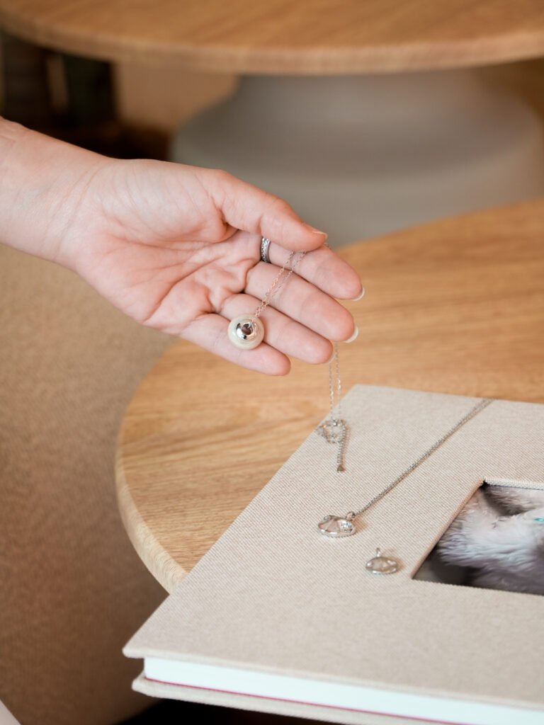Silver pet memorial necklace held over a keepsake photo album at Furwell